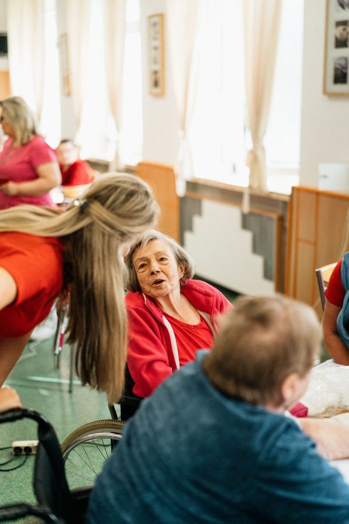 services-03 Elderly woman in a wheelchair engaging with caregiver in a bright, welcoming environment.