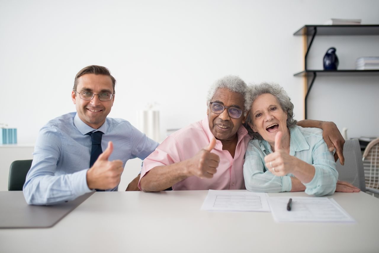 about-02 Elderly couple with consultant giving thumbs up in an office setting, showcasing positive interaction.